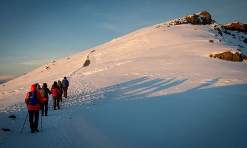 A group of hikers trekking a snowy mountain path at sunrise.