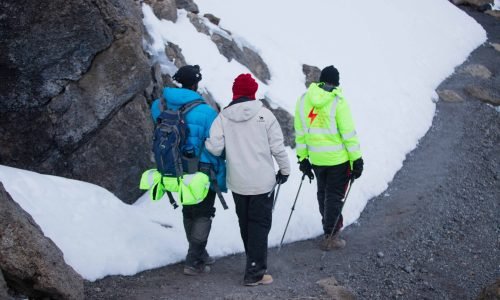 Three hikers navigate a snowy mountain trail, equipped with winter gear.