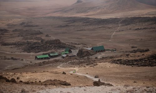 High-angle shot of hikers approaching a remote mountain base camp with rugged terrain.